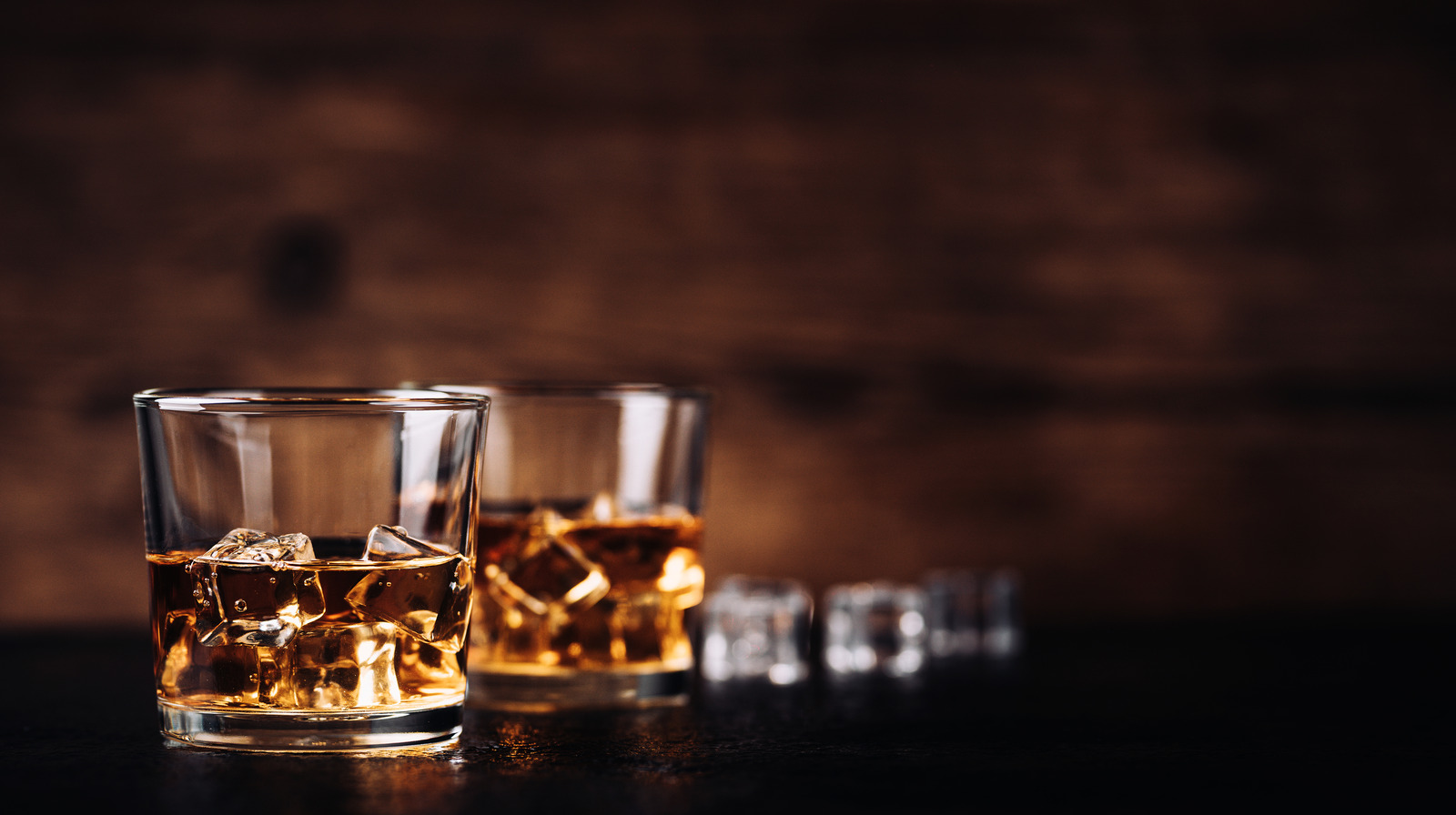 Whiskey or bourbon in a rocks glass with a big ice cube, shot with hard  light and harsh shadows, pink tile backdrop, copy space Stock Photo