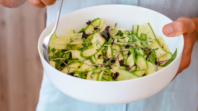 hands holding bowl of zucchini noodles