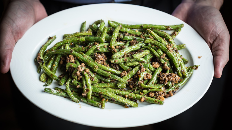 Hands holding a plate of gan bian si ji dou