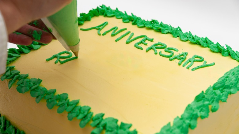 A person writing on a yellow cake with green icing