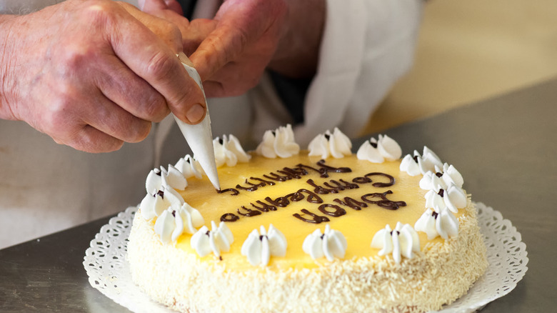 A person writing on a cake with a mini piping bag