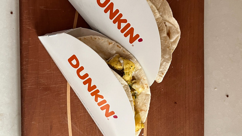 Two tacos in wrappers on cutting board