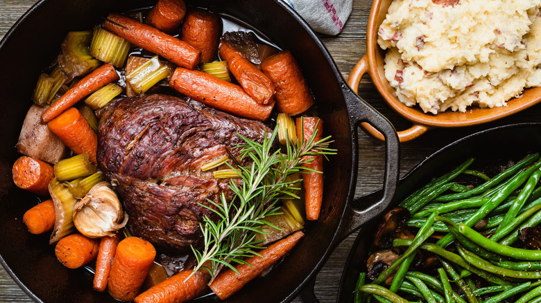 Meat and carrots in a dutch oven next to beans and potatoes