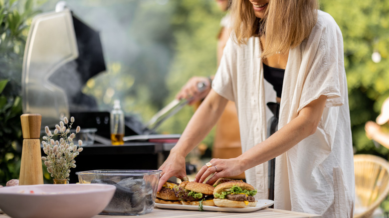 A woman preparing a plate of burgers outside by a grill