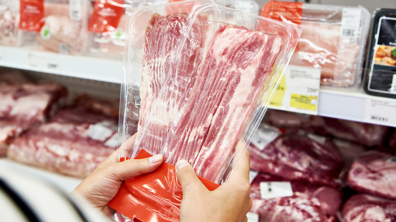 shopper holding up packaged bacon in store