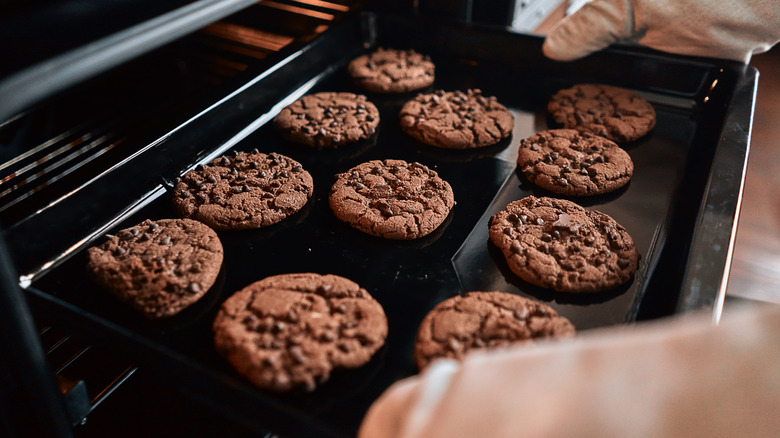 hands taking tray of cookies out of oven