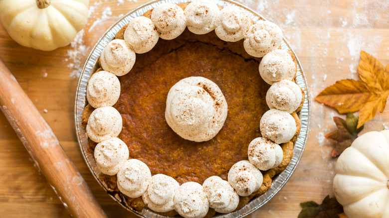 Homemade pumpkin pie in a festive setting with small white pumpkin decorations