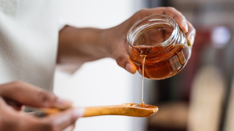 Pouring a jar of honey onto a wooden spoon