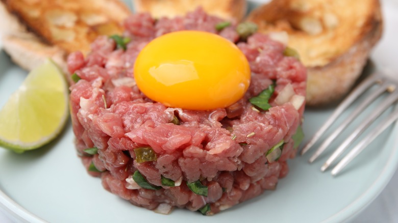 Steak tartare served with confit egg toasted bread and a lime wedge