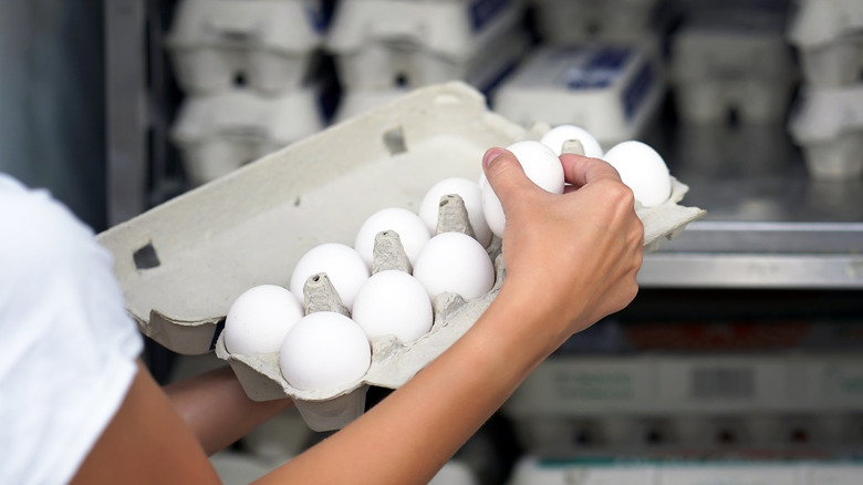 Person holding open carton of eggs in front of a refrigerator