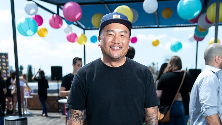 Roy Choi smiling outdoors in a black tee shirt with blue, pink and blue balloons behind him