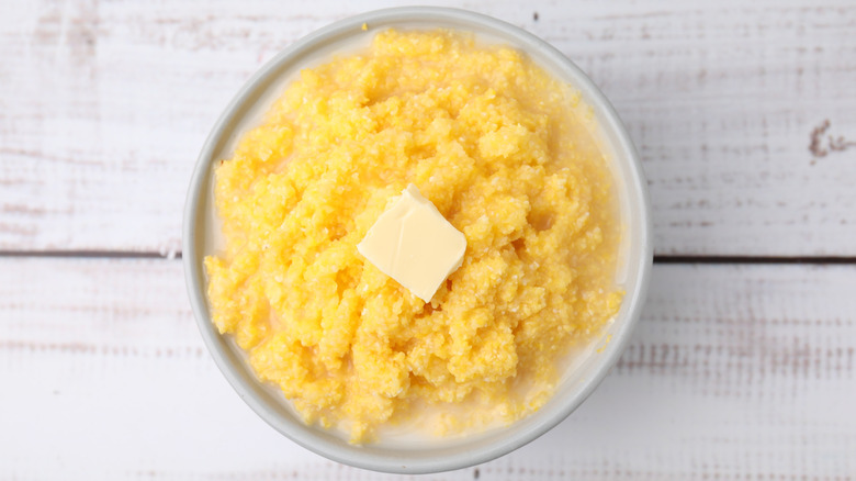 Overhead shot of a bowl of plain grits with butter on a white wood table