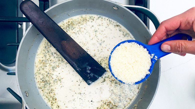 hand holding parmesan cheese over cream sauce