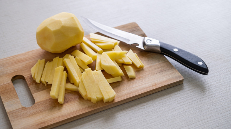 Peeled potatoes cut into fries on wooden board