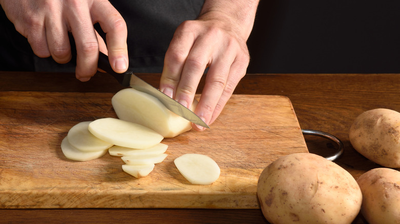 Person slicing potatoes on wooden board