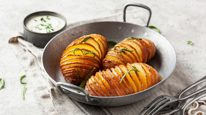 Hasselback potatoes in metal pan with sour cream dipping sauce