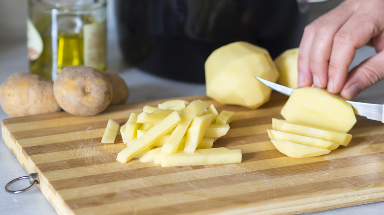 Person cutting french fries on wooden board