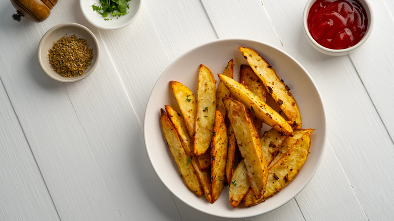 Bowl of potato wedges with tomato ketchup and seasonings