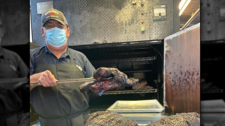 Man apron hat mask holding smoked meat