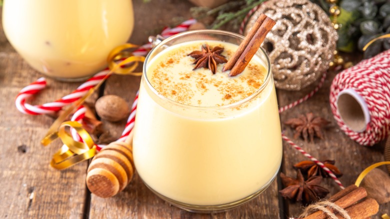 Glass of eggnog with an anise star and cinnamon stick surrounded by Christmas decor