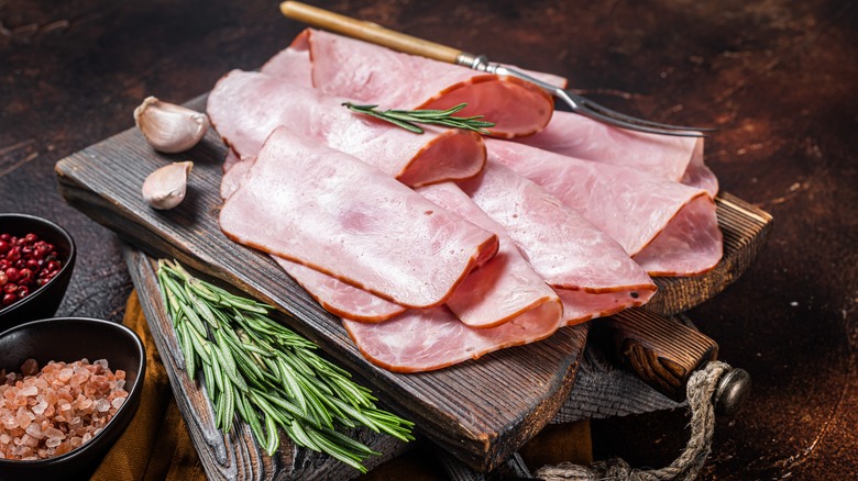 Ham on a cutting board surrounded by herbs