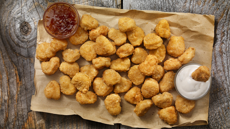 Chicken nuggets on parchment paper on a wood tabletop with dipping sauces