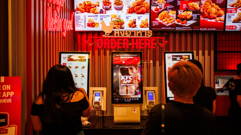 Vivid red KFC ordering area with customers placing orders on screens