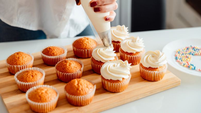 Person frosting cupcakes using a piping bag