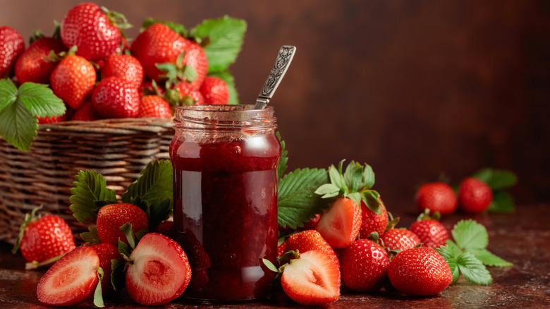 Fresh strawberries in a basket and surrounding a glass jar of jam.