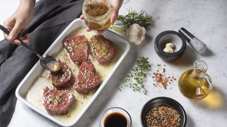 A person preparing steaks by adding a marinade of oil and spices.