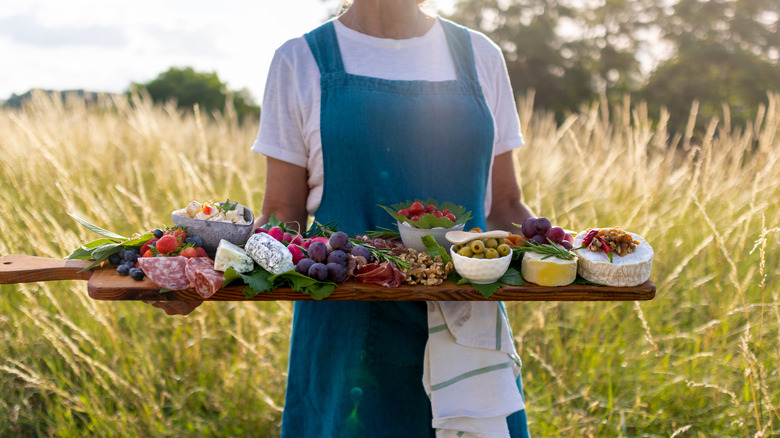 Woman in a grassy field holding a charcuterie board