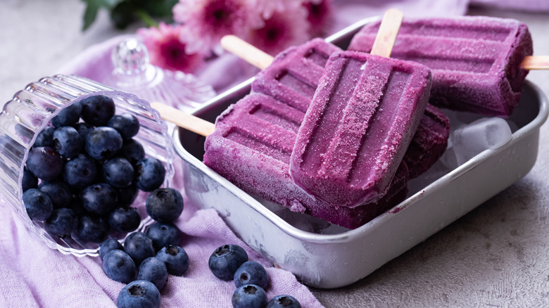 Creamy blueberry popsicles on a platter next to a bowl of blueberries