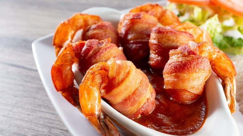 bacon wrapped shrimp hooked over a dish of cocktail sauce