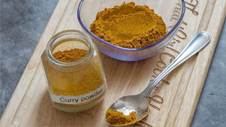 glass jar, glass dish and teaspoon of Jamaican curry powder