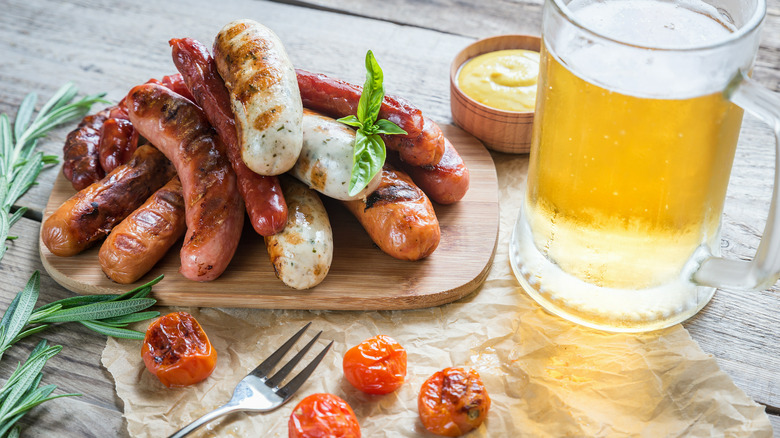 Pile of grilled brats on a cutting board with beer