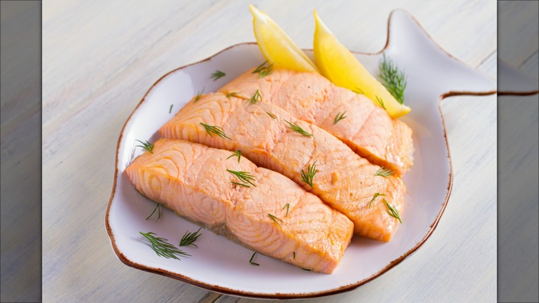 Poached salmon filet on white plate with dill and lemon wedges