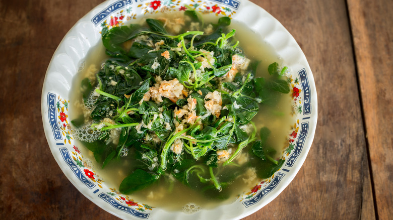 A bowl of brothy soup with leafy greens