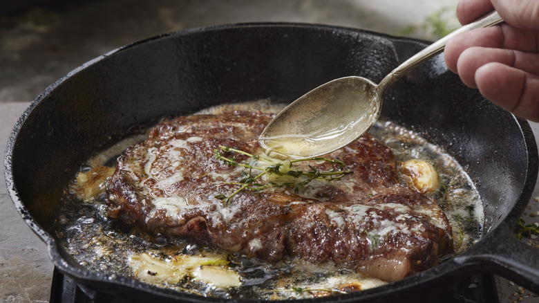 Fat being spooned onto steak in a skillet