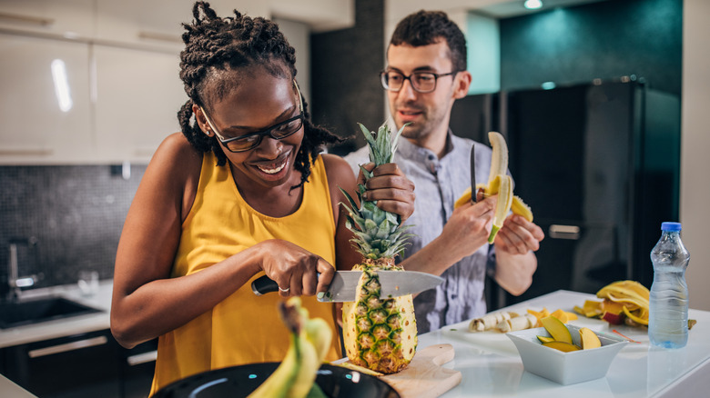 A smiling woman cutting a pineapple