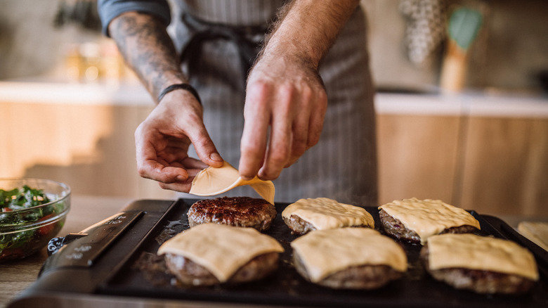 chef putting cheese on burgers