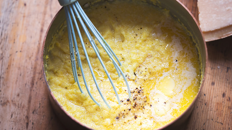 cooked grits in pot with whisk on wooden table