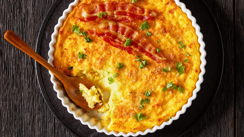 grit casserole with bacon in white dish  on wooden table with spoon