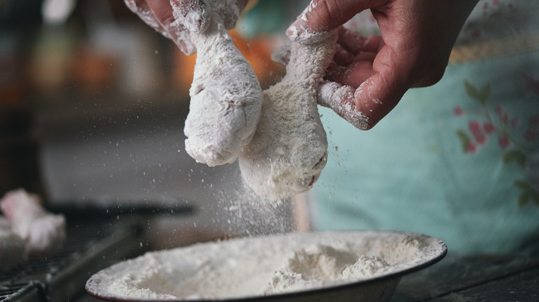 Hands coating chicken in flour