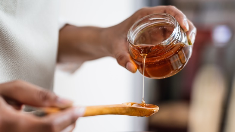 Person pouring honey onto wooden spoon