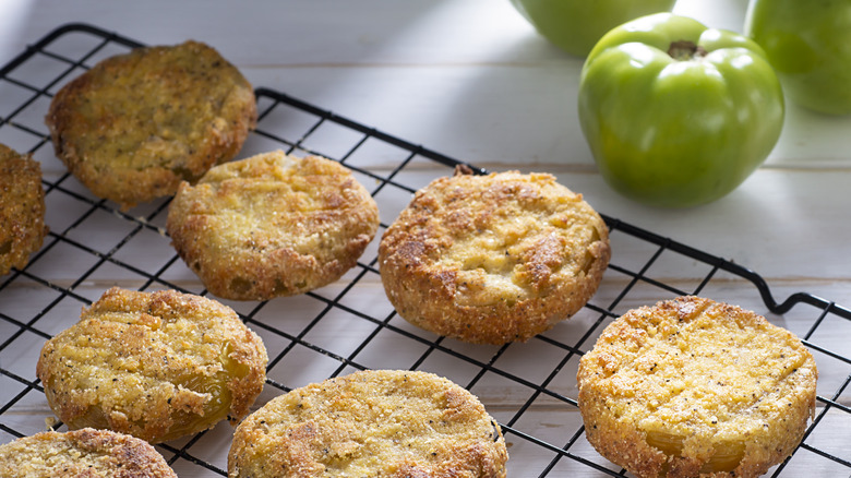 fried green tomatoes on a wire rack next to whole tomatoes