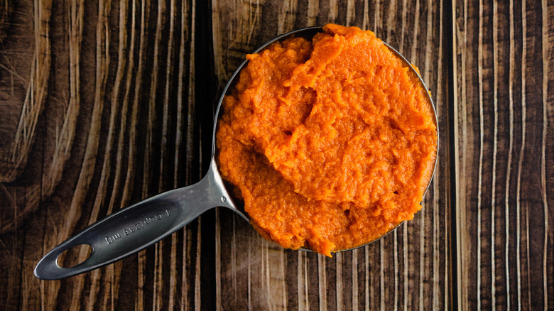 measuring cup full of canned pumpkin puree on wood background