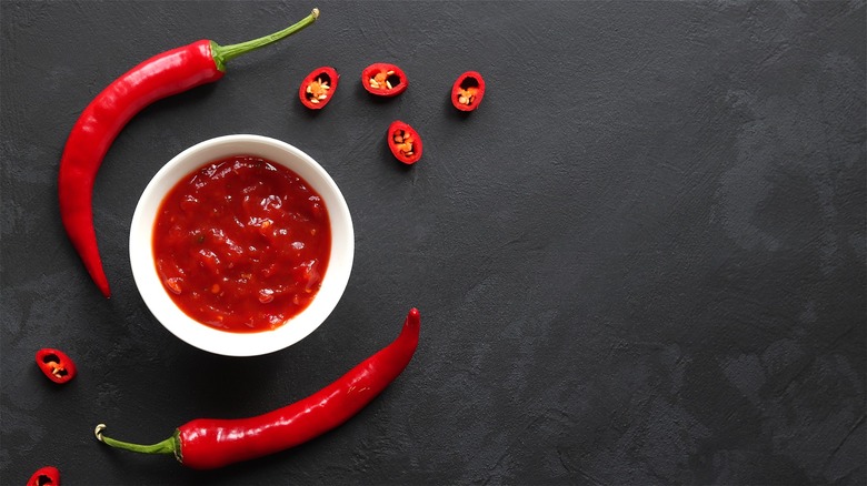 Whole and chopped red chili peppers on counter with dish of jelly