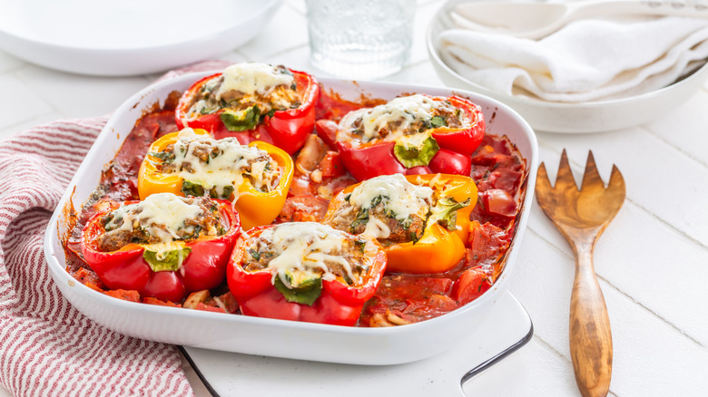 Baked stuffed peppers in a dish surrounded by a red sauce.