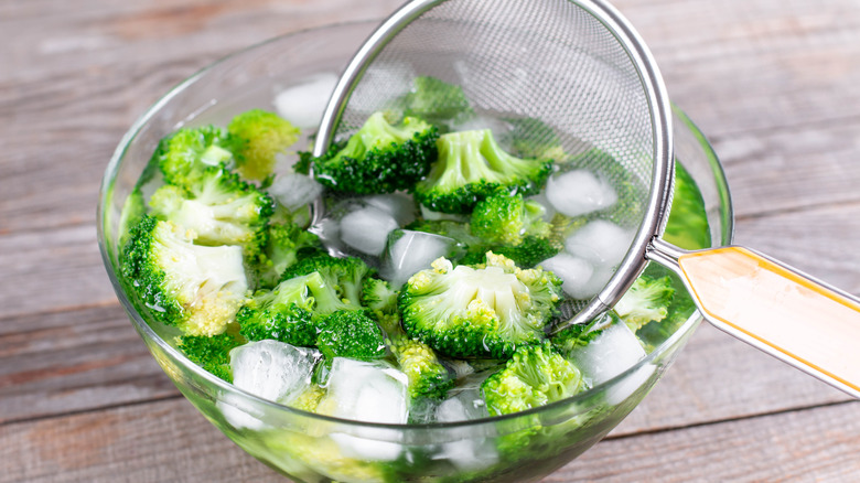 blanched broccoli being submerged in bowl of ice water