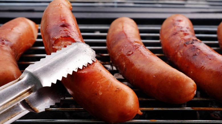 tongs flipping sausages on grill